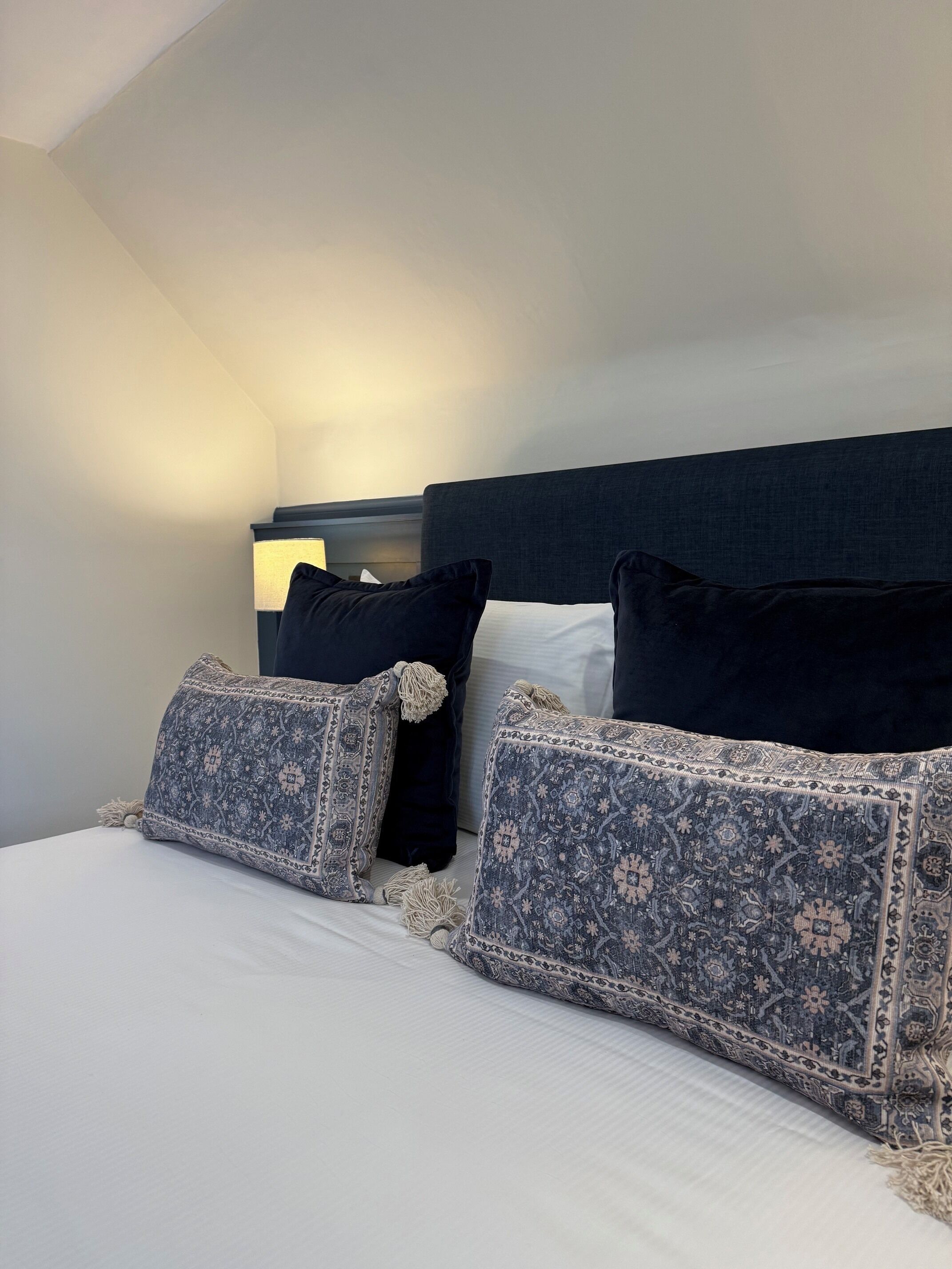A neatly made bed with patterned pillows and a dark headboard in a hotel room.