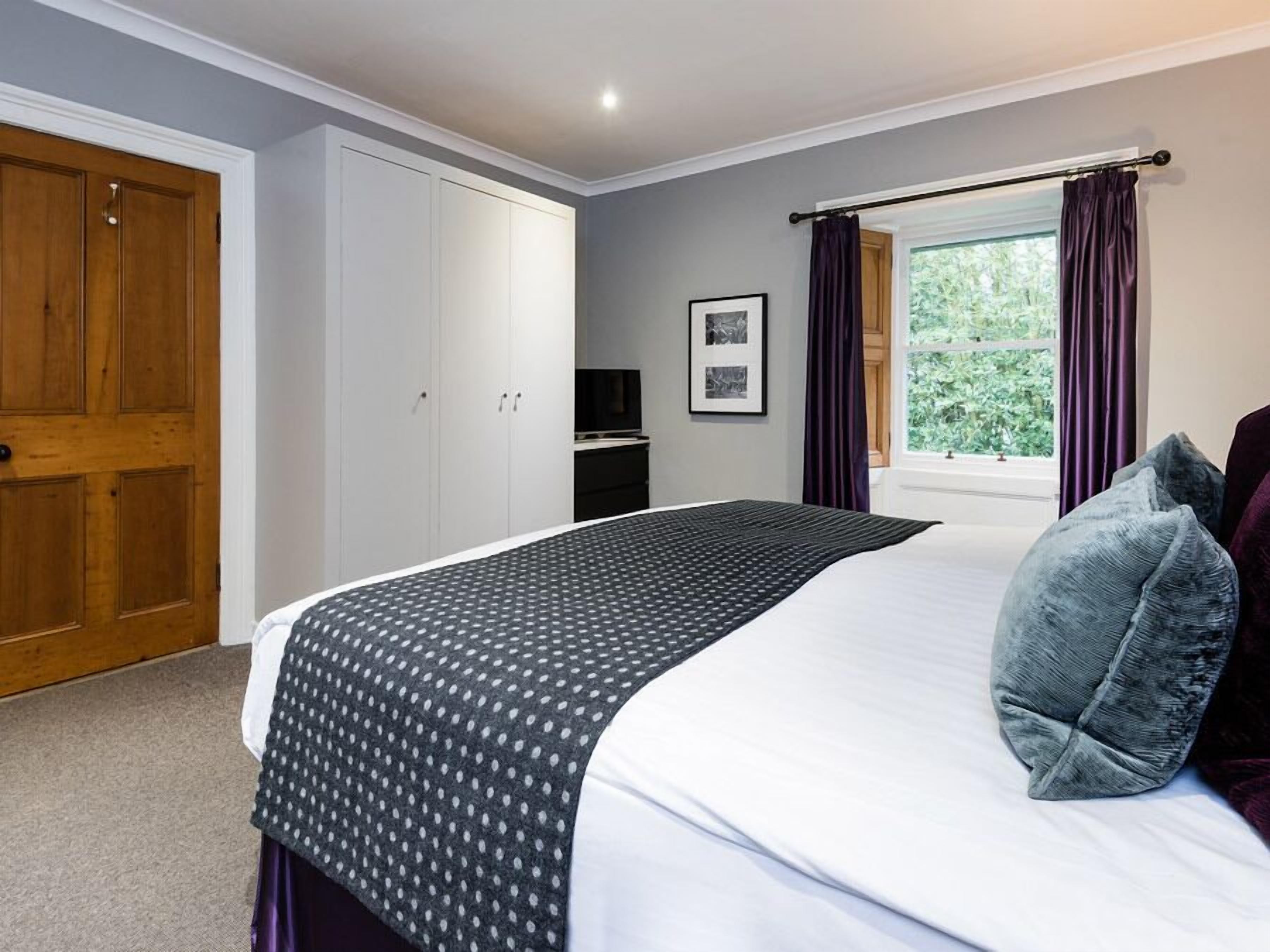 A bedroom with a bed, a wardrobe, a television, and a window with curtains.
