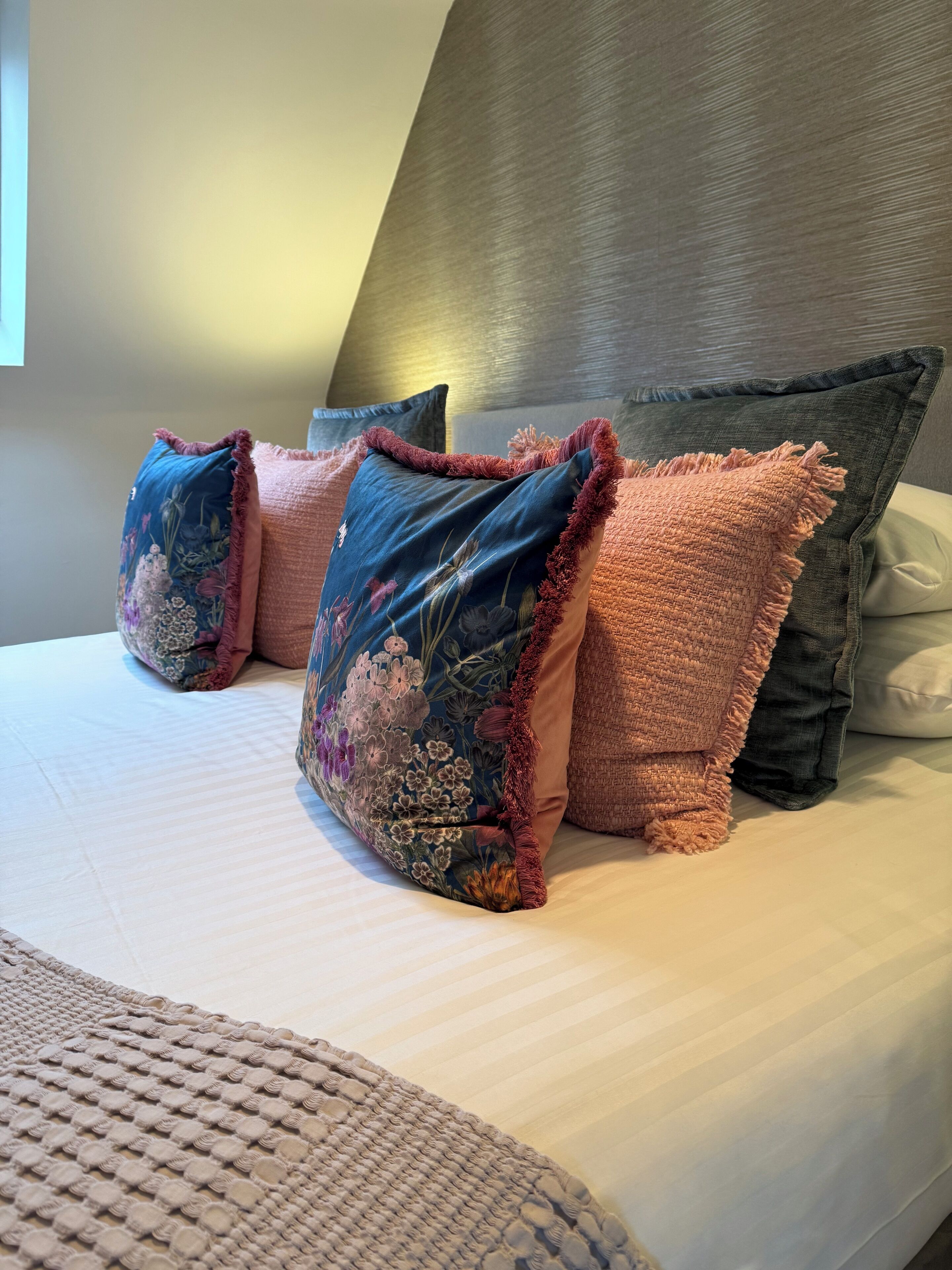 Un letto con una lenzuola bianca e quattro cuscini decorativi.
