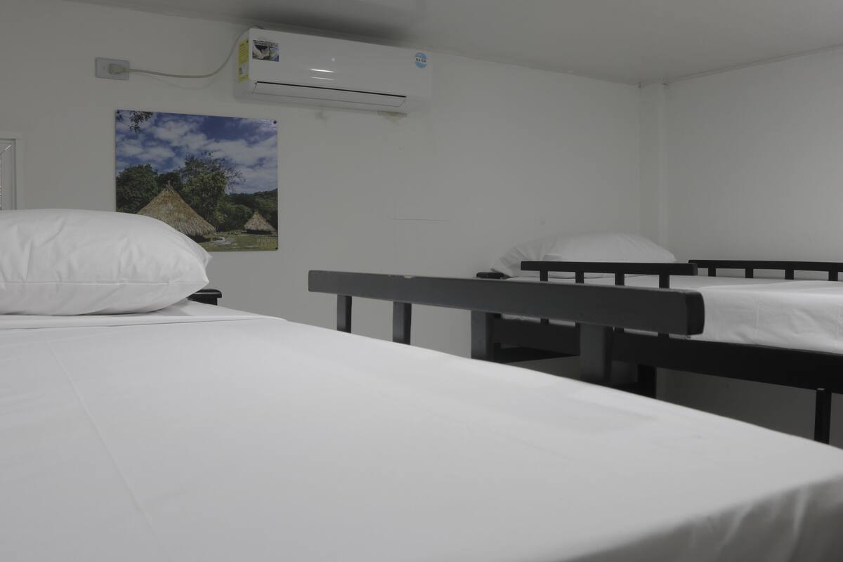 Une chambre d’hôtel avec deux lits simples, du linge de lit blanc, un climatiseur fixé au mur et un tableau représentant un paysage tropical.