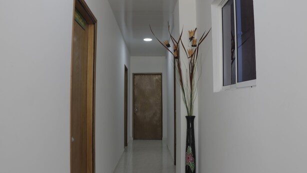 A hallway with a wooden door labeled "URITACA," a potted plant, and a window with blinds. - Puerto Caribe Hostal (Santa Marta)