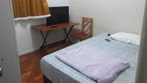 Une petite pièce comprenant un lit, un bureau avec un ordinateur, une chaise et une fenêtre avec des rideaux.