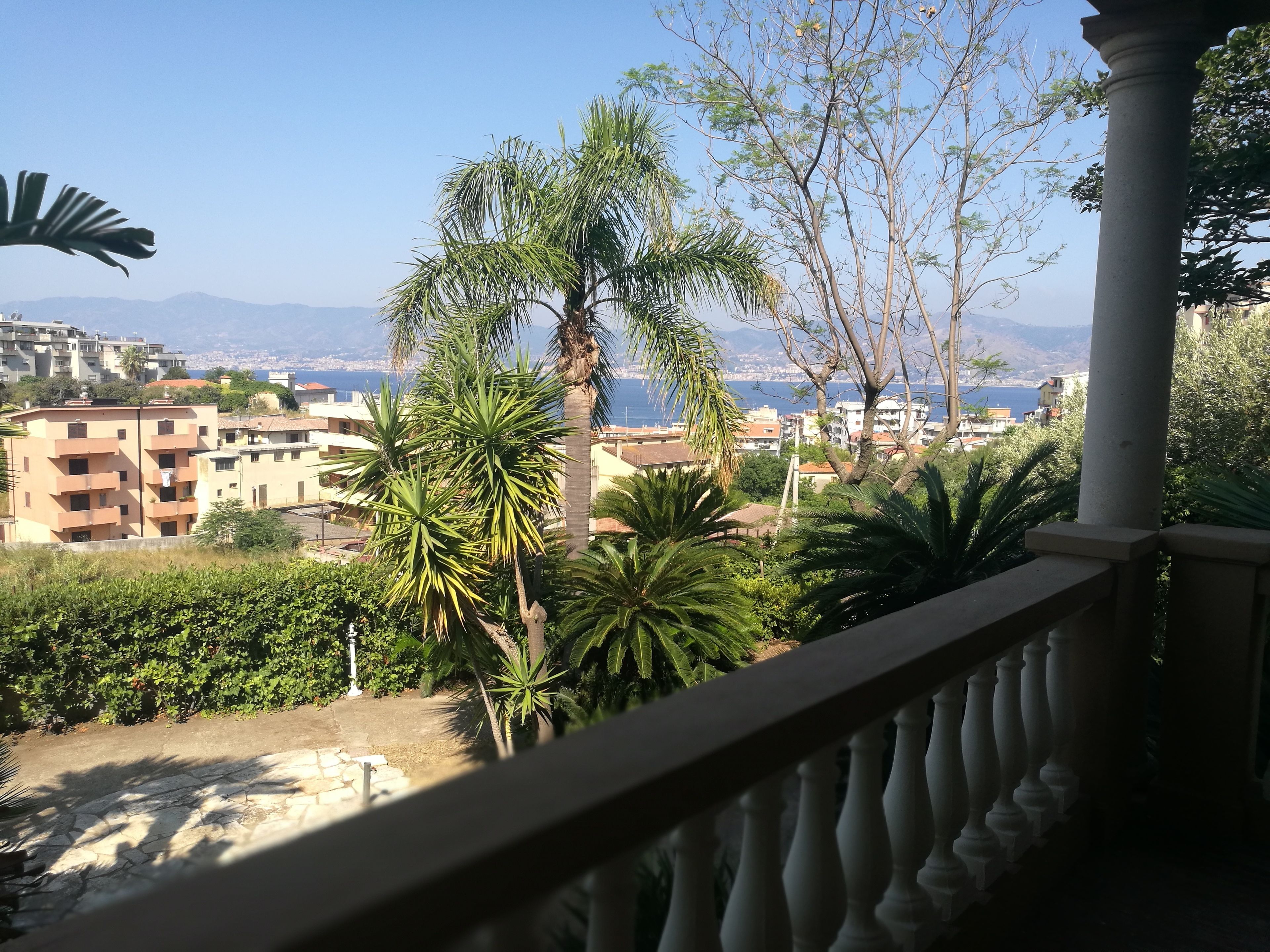 A balcony with a view of a coastal cityscape, including buildings and a body of water.