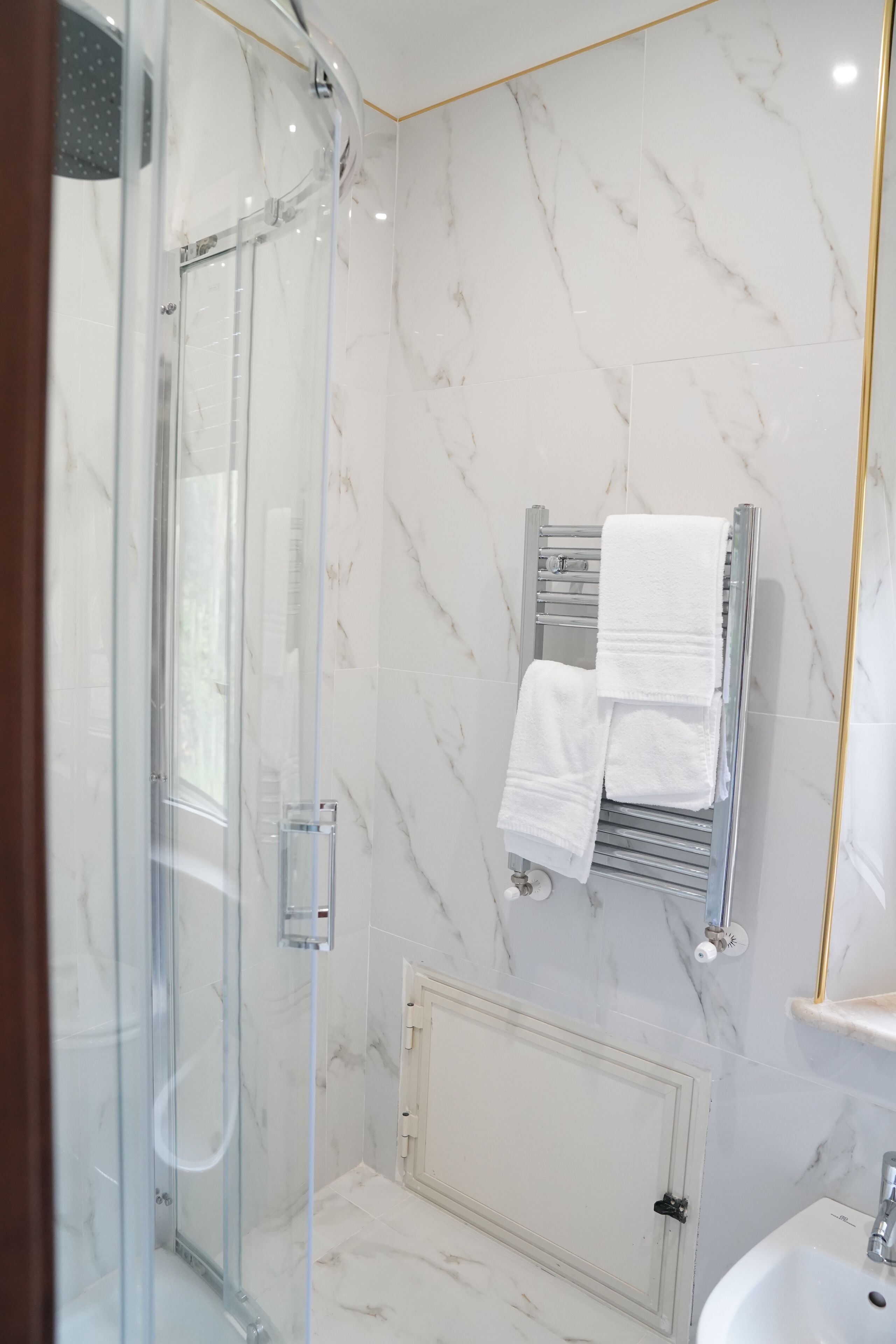 Une salle de bain moderne avec une douche à parois de verre, un mur en marbre blanc, un porte-serviettes et un lavabo blanc.