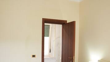 A hotel room with a bed, a desk, a chair, a nightstand, a lamp, and a bathroom visible through an open door.