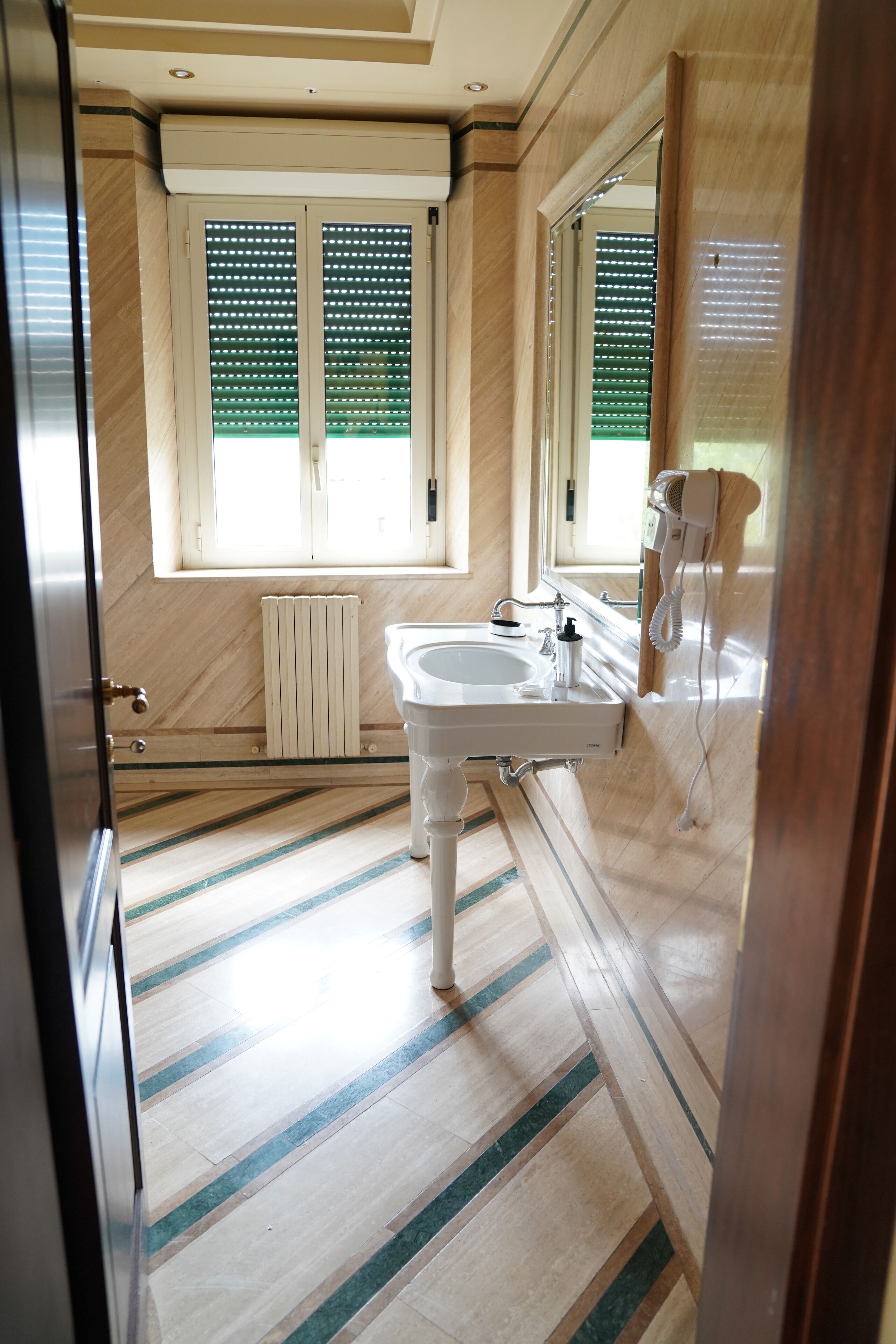 Ein Badezimmer mit großem Fenster, Heizkörper, Waschbecken und einem an der Wand befestigten Fön.