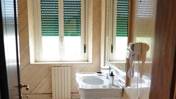Ein Badezimmer mit großem Fenster, Heizkörper, Waschbecken und einem an der Wand befestigten Fön.
