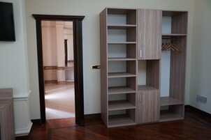 Una habitación con piso de madera, un armario con varios estantes y una puerta que da a otra habitación.