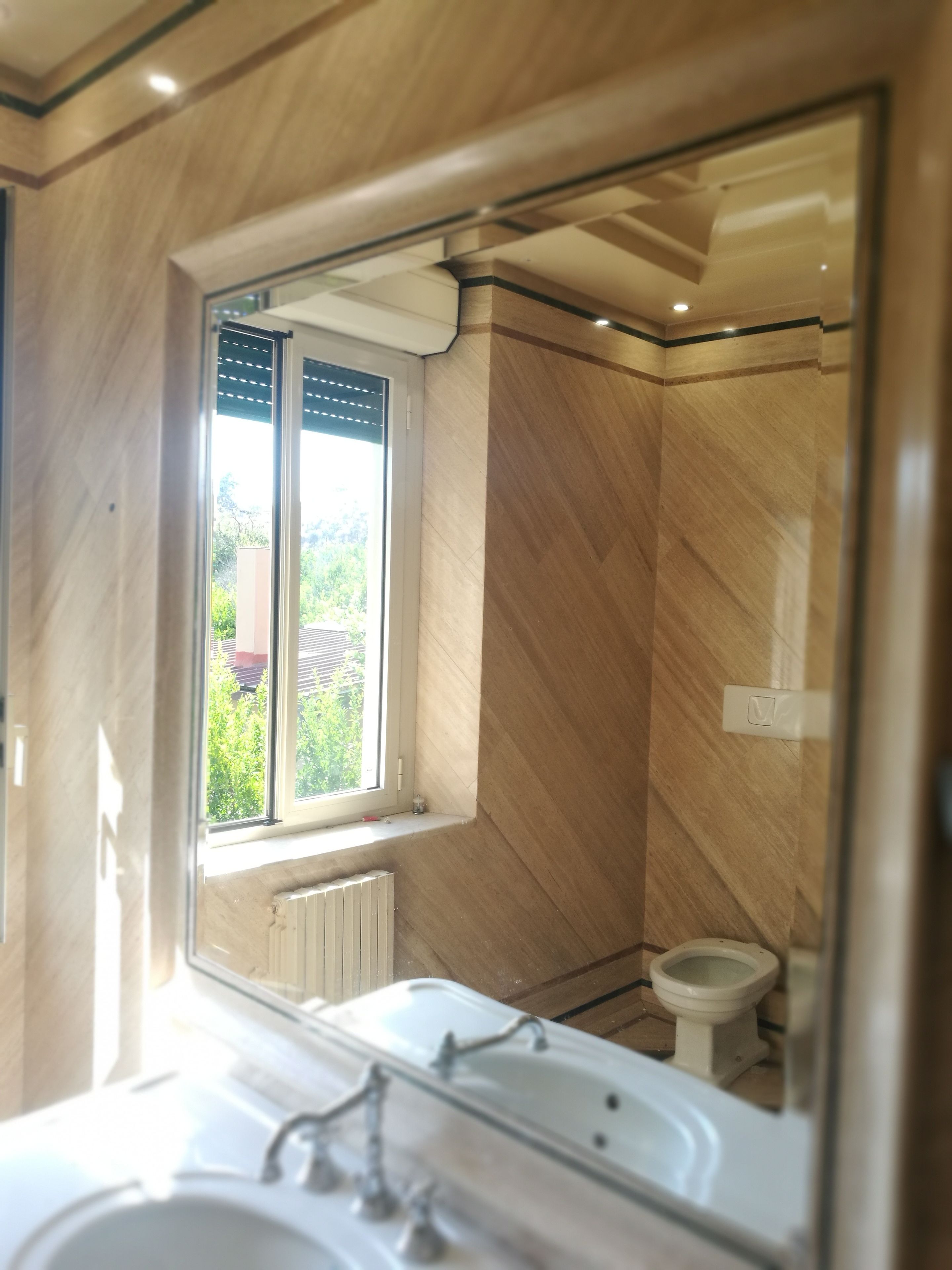 Une salle de bain dotée d’un grand miroir, d’une baignoire, de toilettes et d’une fenêtre donnant sur un paysage verdoyant.