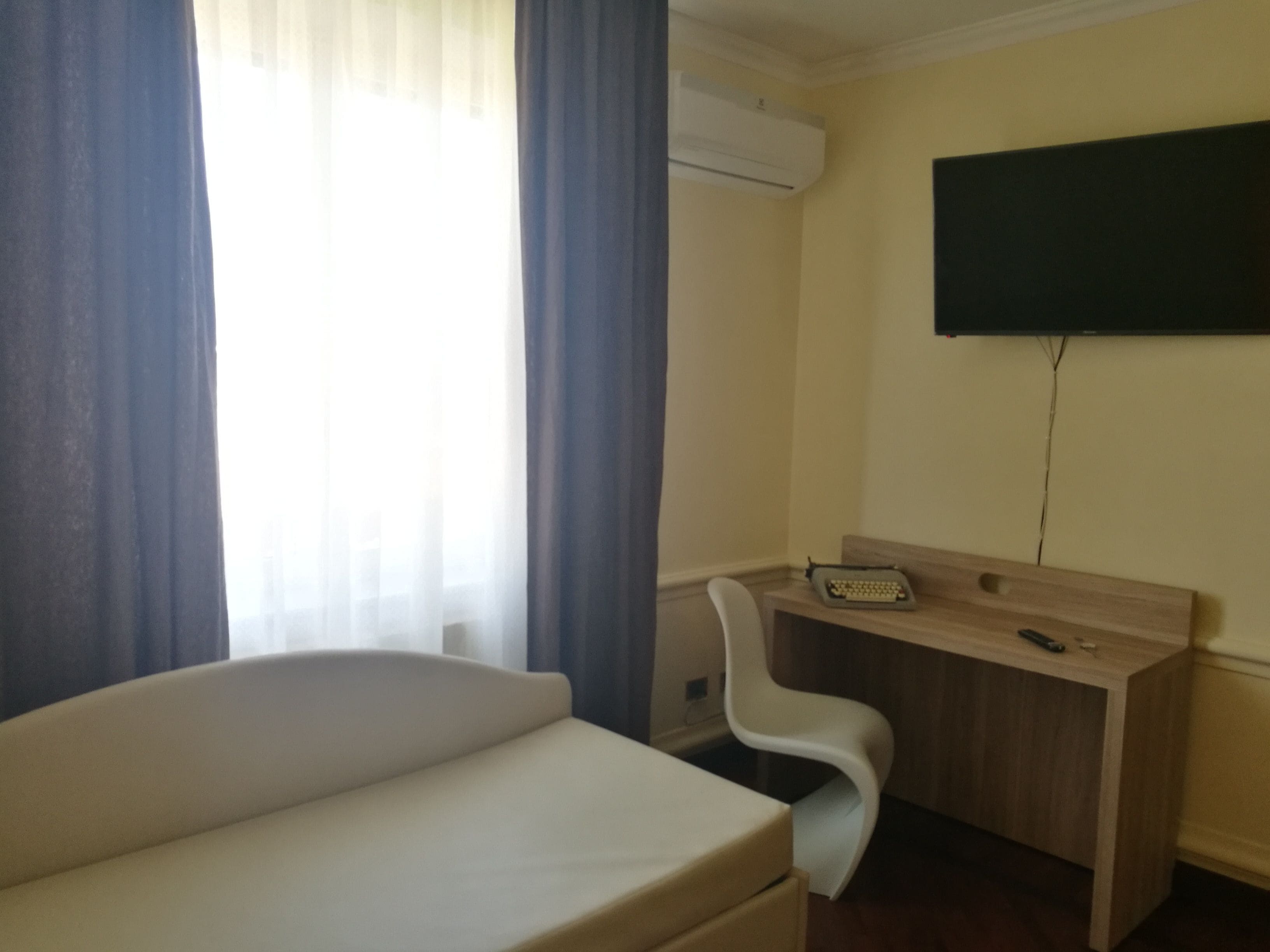 Una habitación con cama, escritorio, silla, televisor montado en la pared y aire acondicionado.