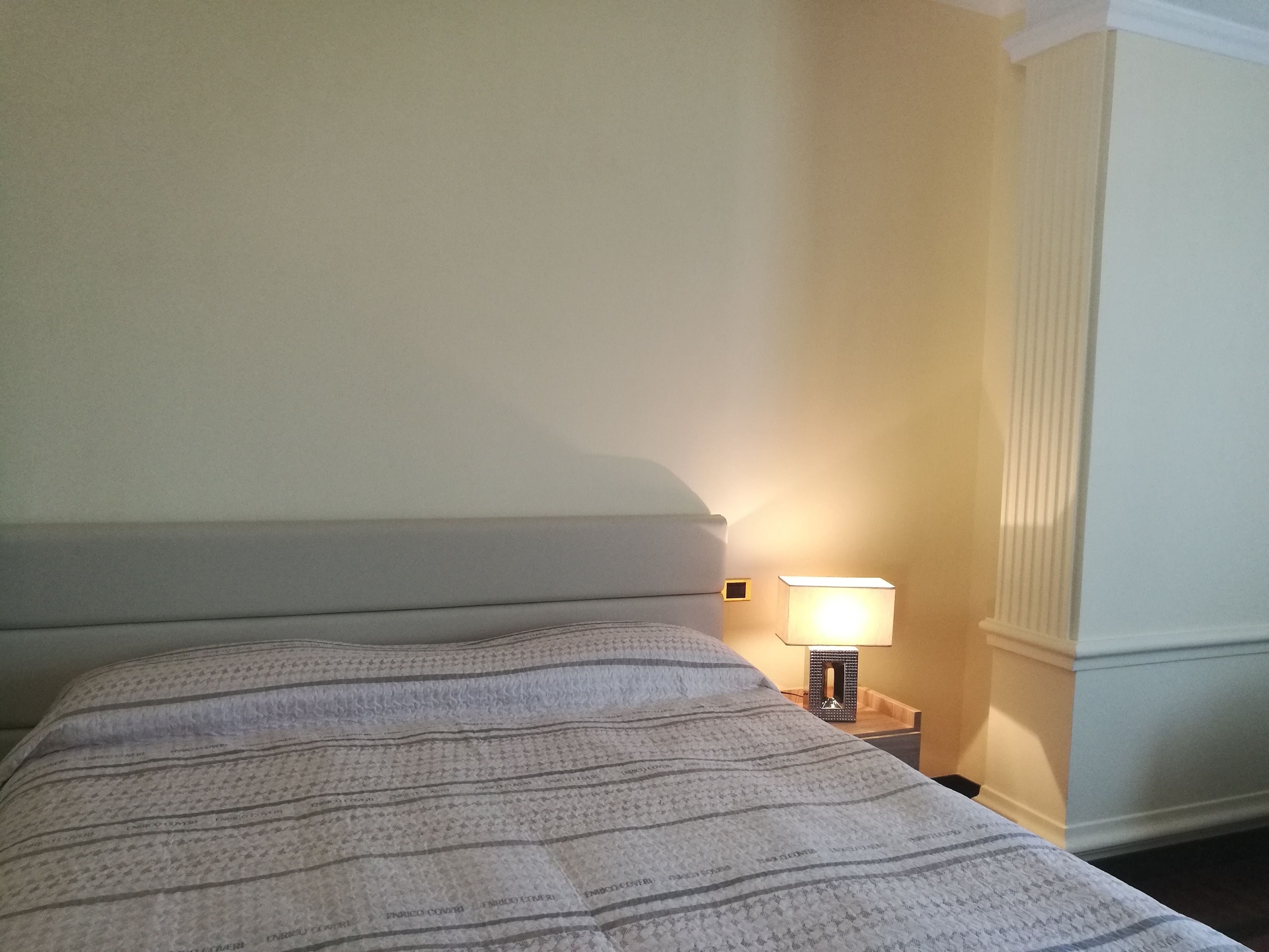 Cama bem arrumada com colcha estampada, luminária de cabeceira e mesa de cabeceira.