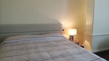Cama bem arrumada com colcha estampada, luminária de cabeceira e mesa de cabeceira.