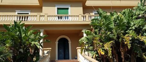 A building with a beige facade, a central entrance with a green door, and a white balustrade.
