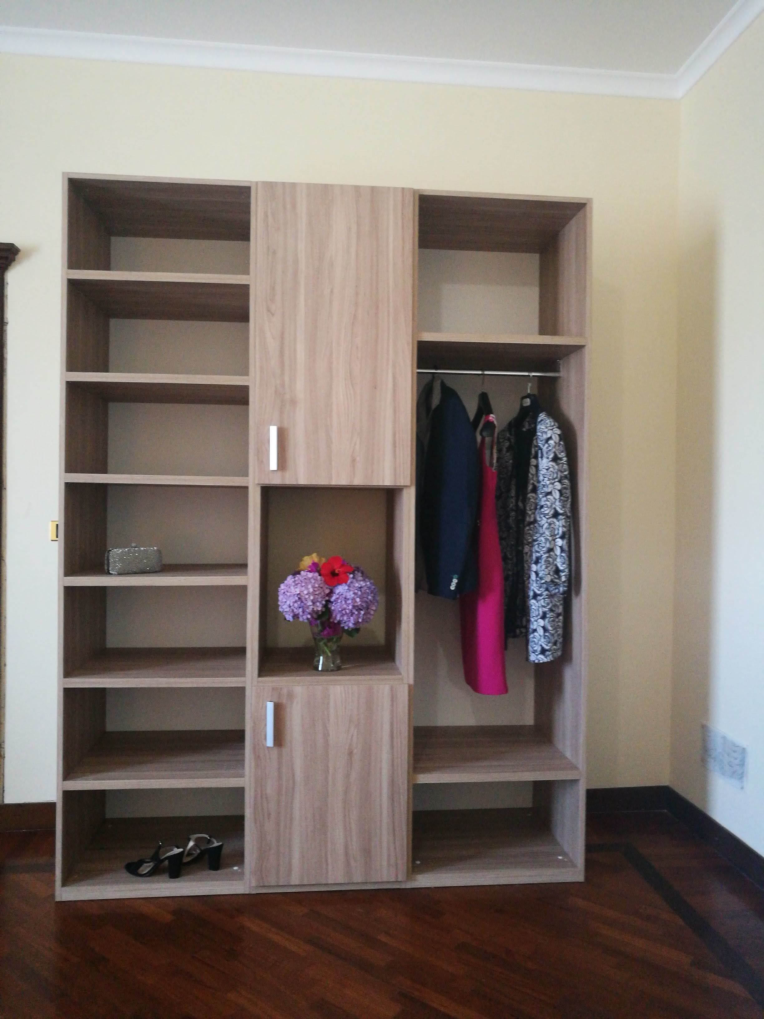 Un armadio in legno con ripiani multipli, una sezione per appendere e un piccolo vaso con fiori.