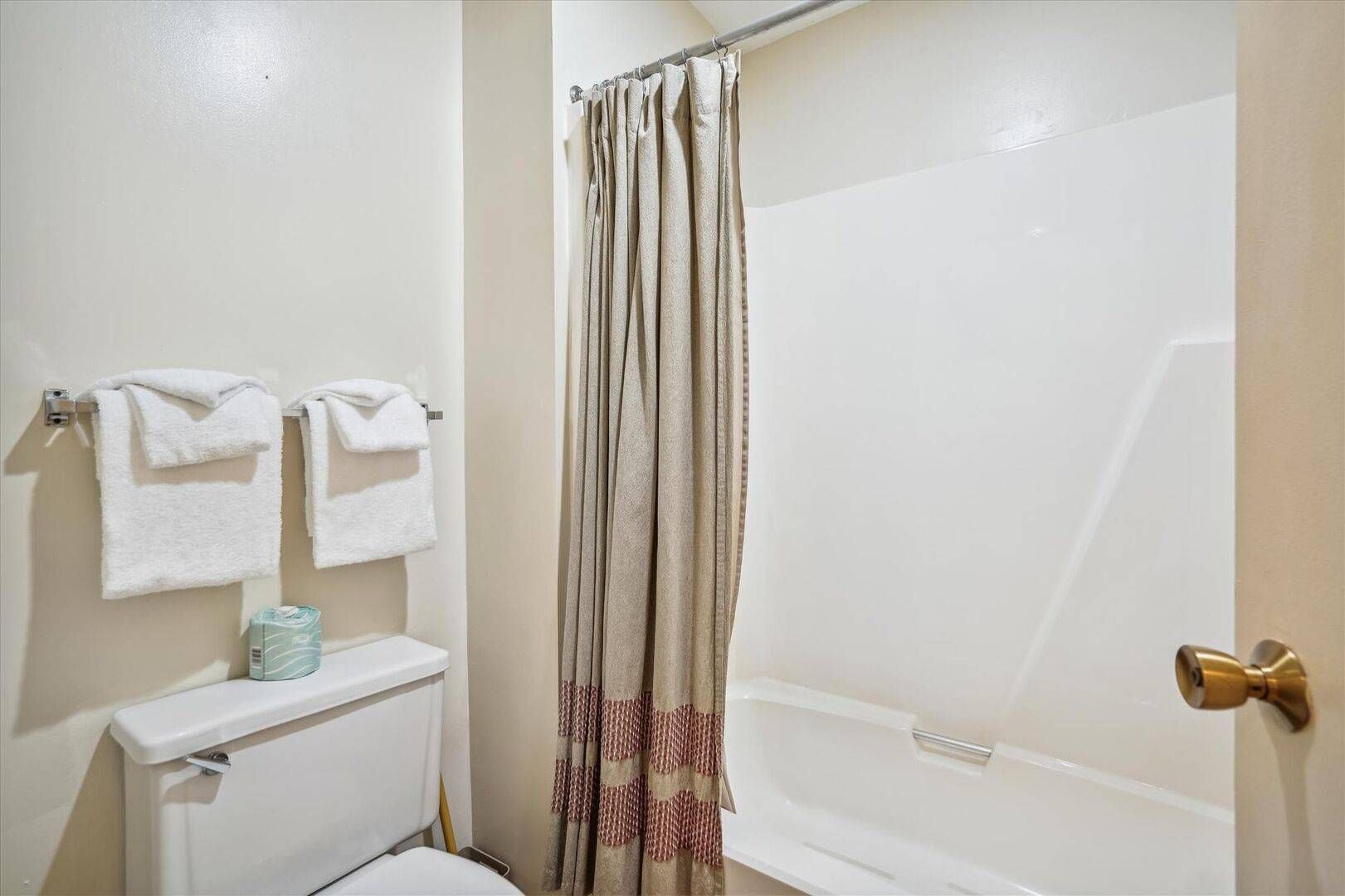 A bathroom with a white toilet, a white sink, a towel rack with two towels, a shower curtain, and a bathtub.