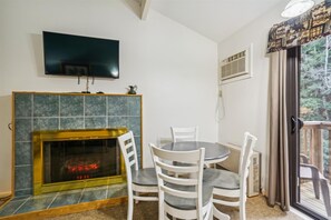 Un comedor con chimenea, un televisor montado encima y vistas al exterior a través de un ventanal.