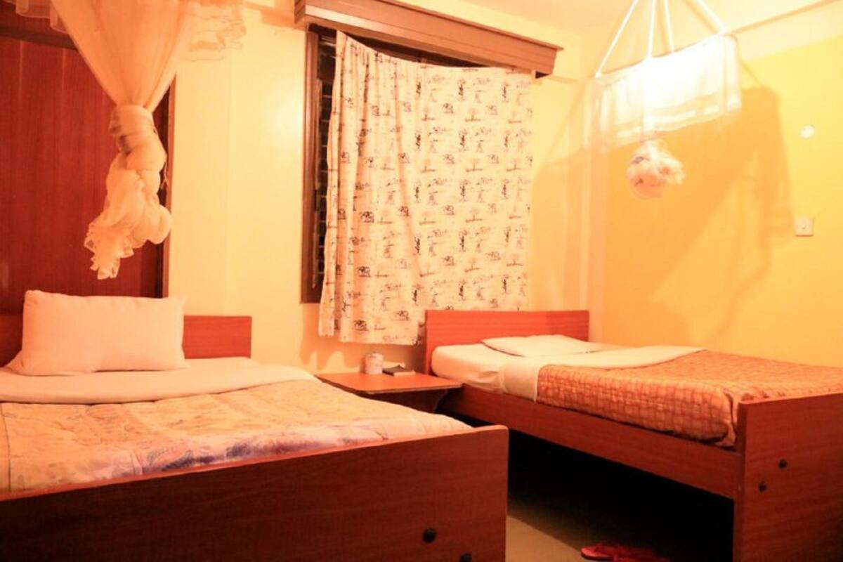 Una habitación con dos camas de madera, un ventanal con cortinas estampadas y una mosquitera colgante.