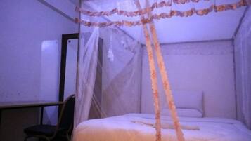 A room with a bed under a canopy, a chair, and a wall-mounted mirror.