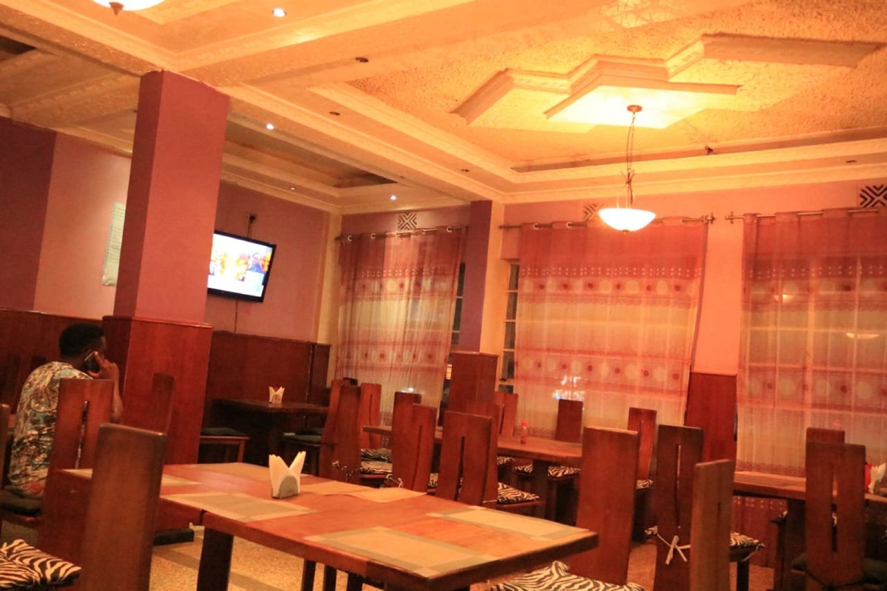 A restaurant with wooden tables and chairs, a television screen, and patterned curtains.