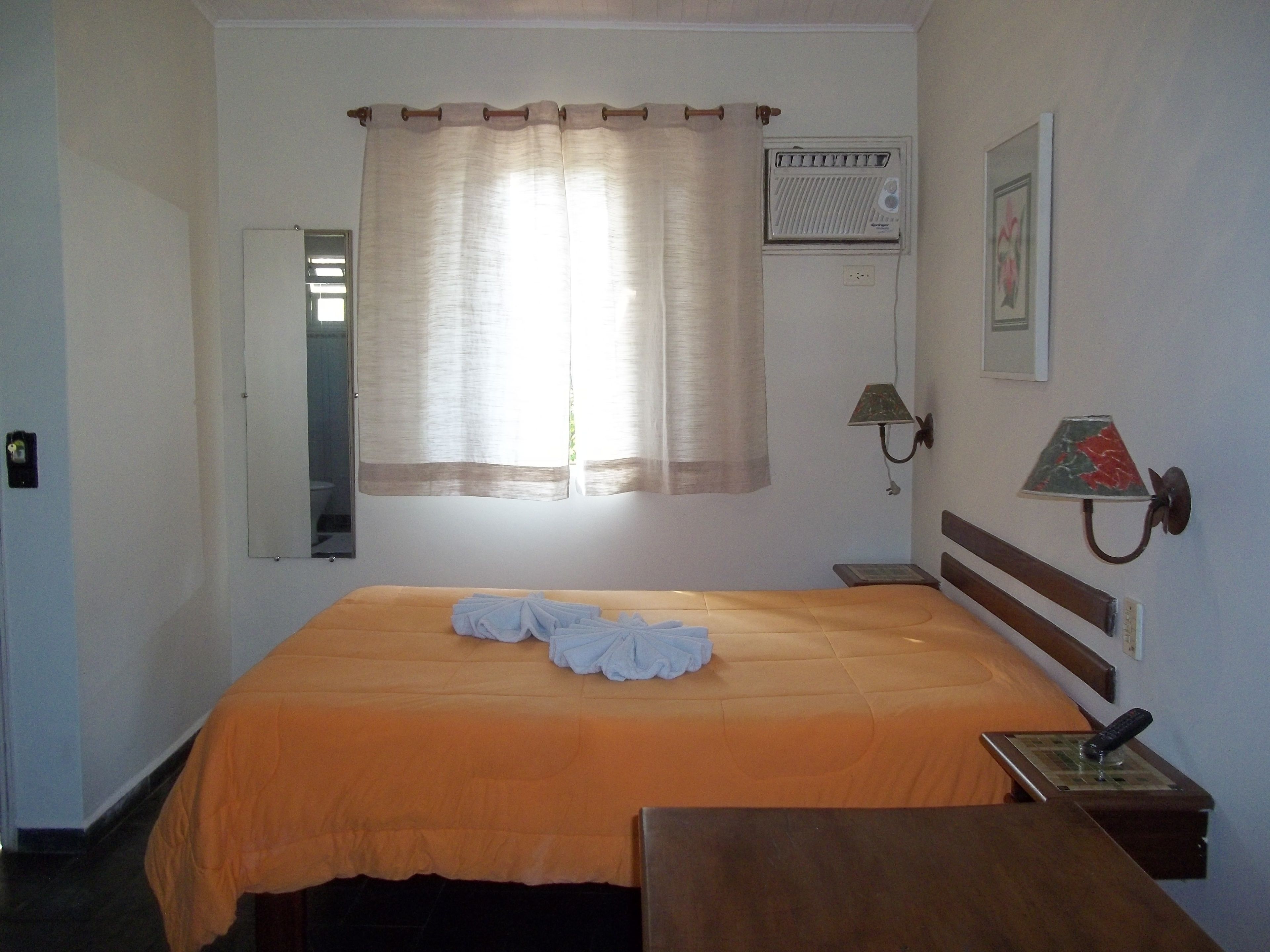 A hotel room with a bed, a bedside table, a lamp, and a wall-mounted heater.