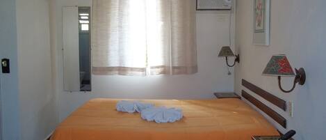 A hotel room with a bed, a bedside table, a lamp, and a wall-mounted heater.