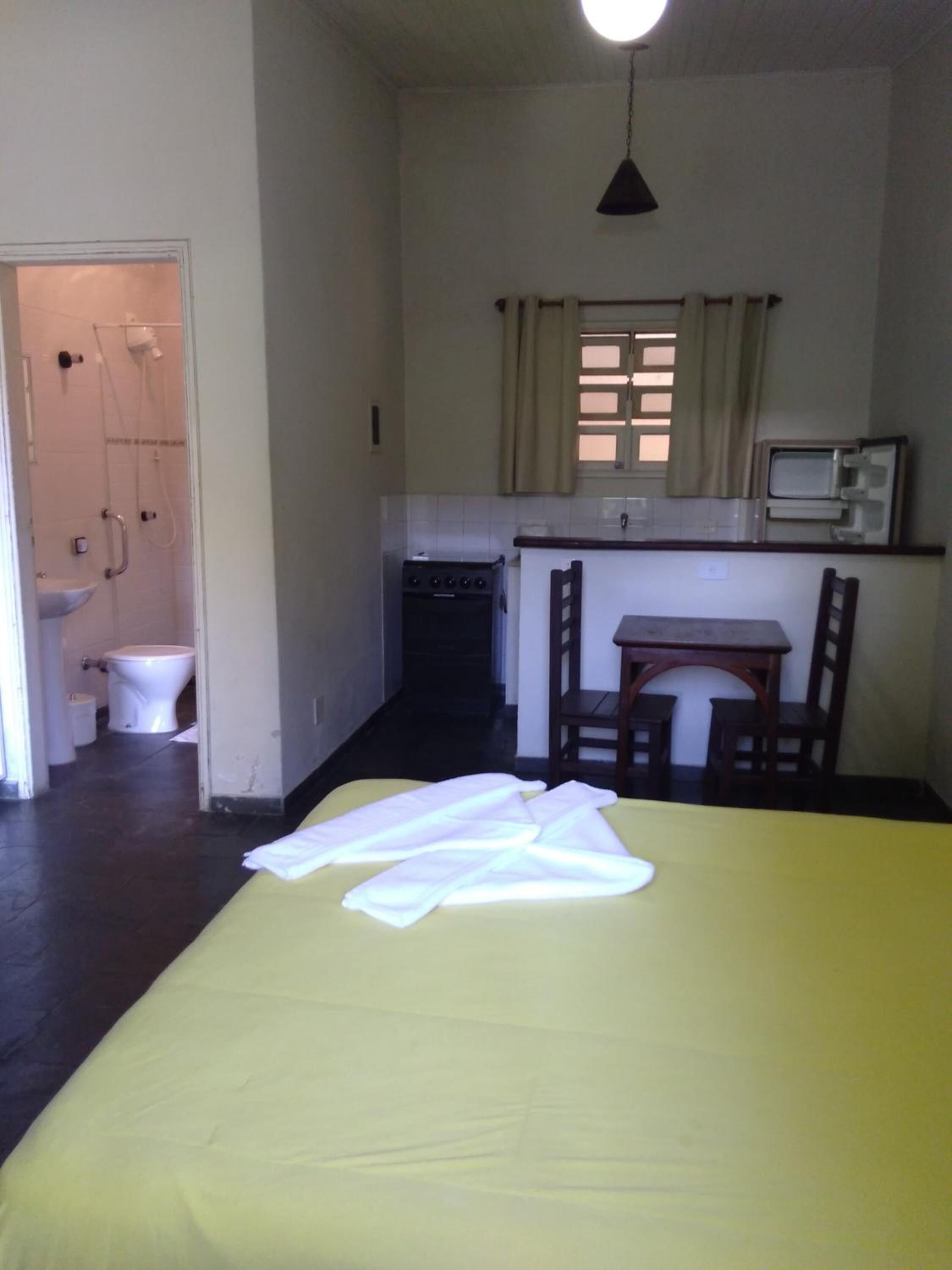 A small, compact room with a bed, a small table, a chair, a microwave, and a sink.