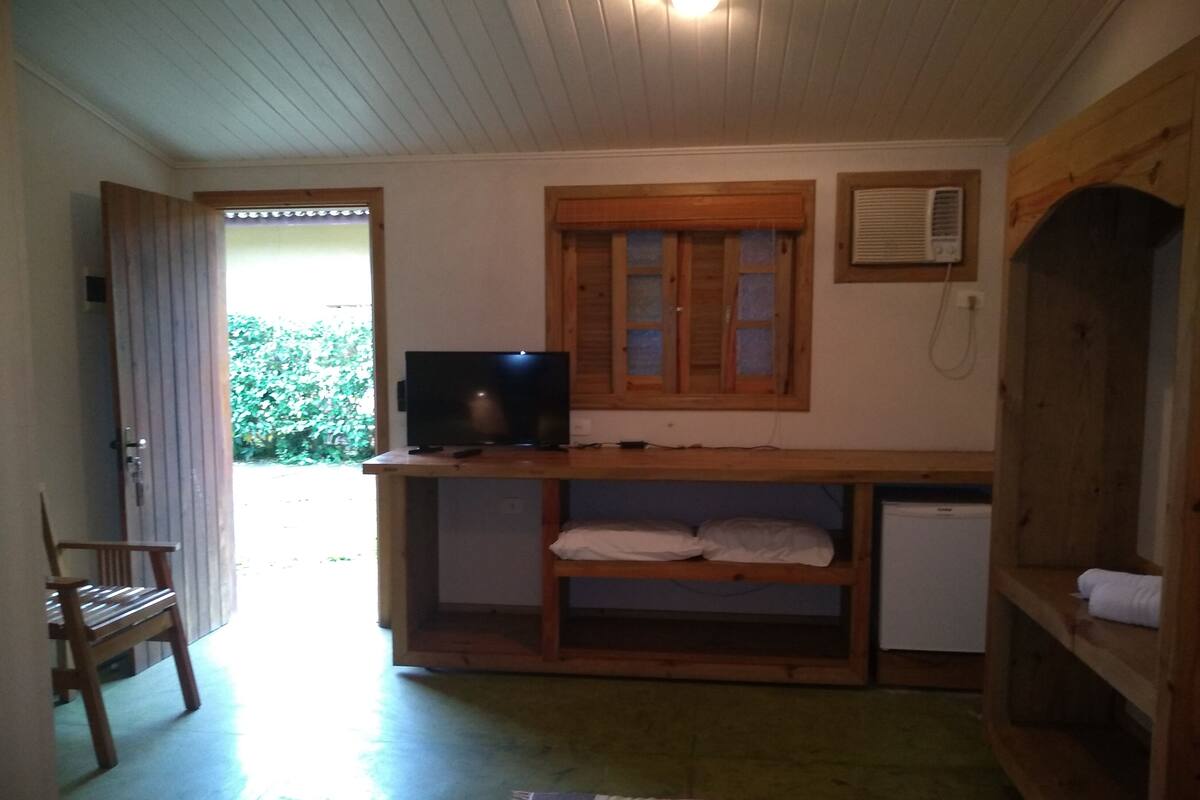 Una habitación pequeña con un escritorio de madera, televisión, refrigerador y un armario de madera.