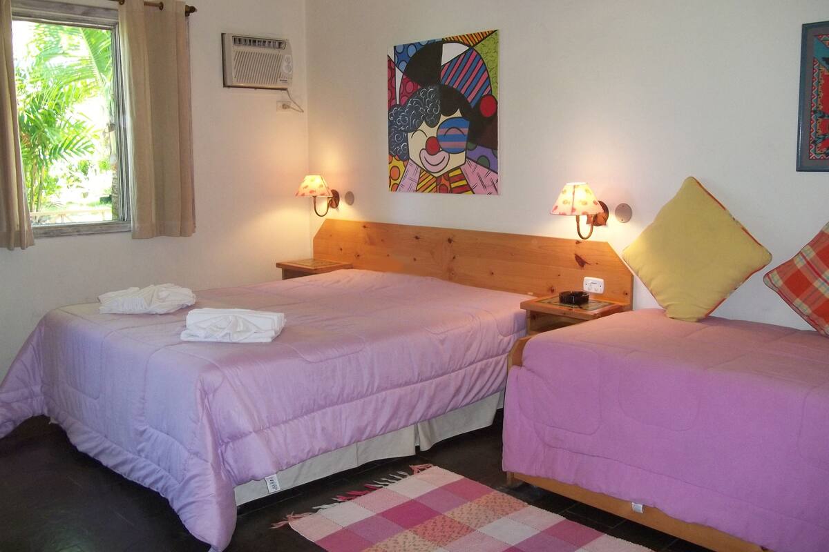 Una habitación con dos camas, cada una con una almohada y una lámpara. Hay una ventana con cortinas, un radiador y un cuadro en la pared.