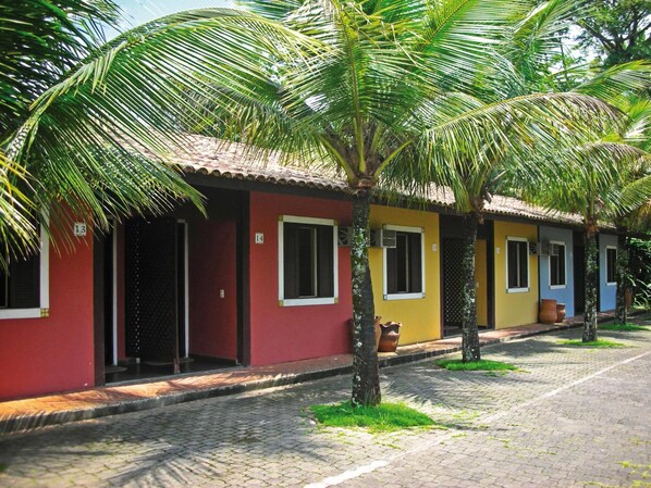 Une rangée de maisons colorées, chacune avec une porte numérotée, une rue pavée et des palmiers.