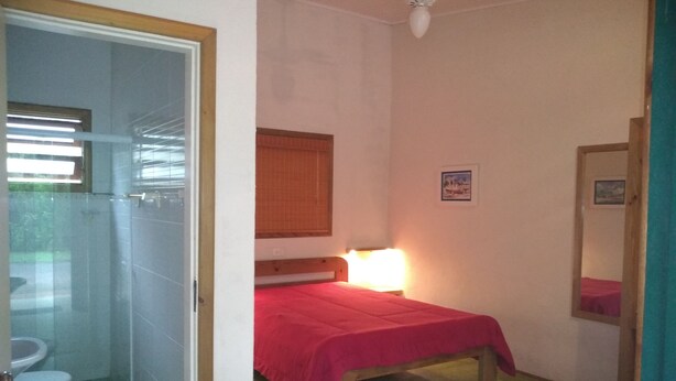 Un alojamiento pequeño de una sola habitación con cama, mesita de noche, espejo, ventana con persianas y zona de ducha.