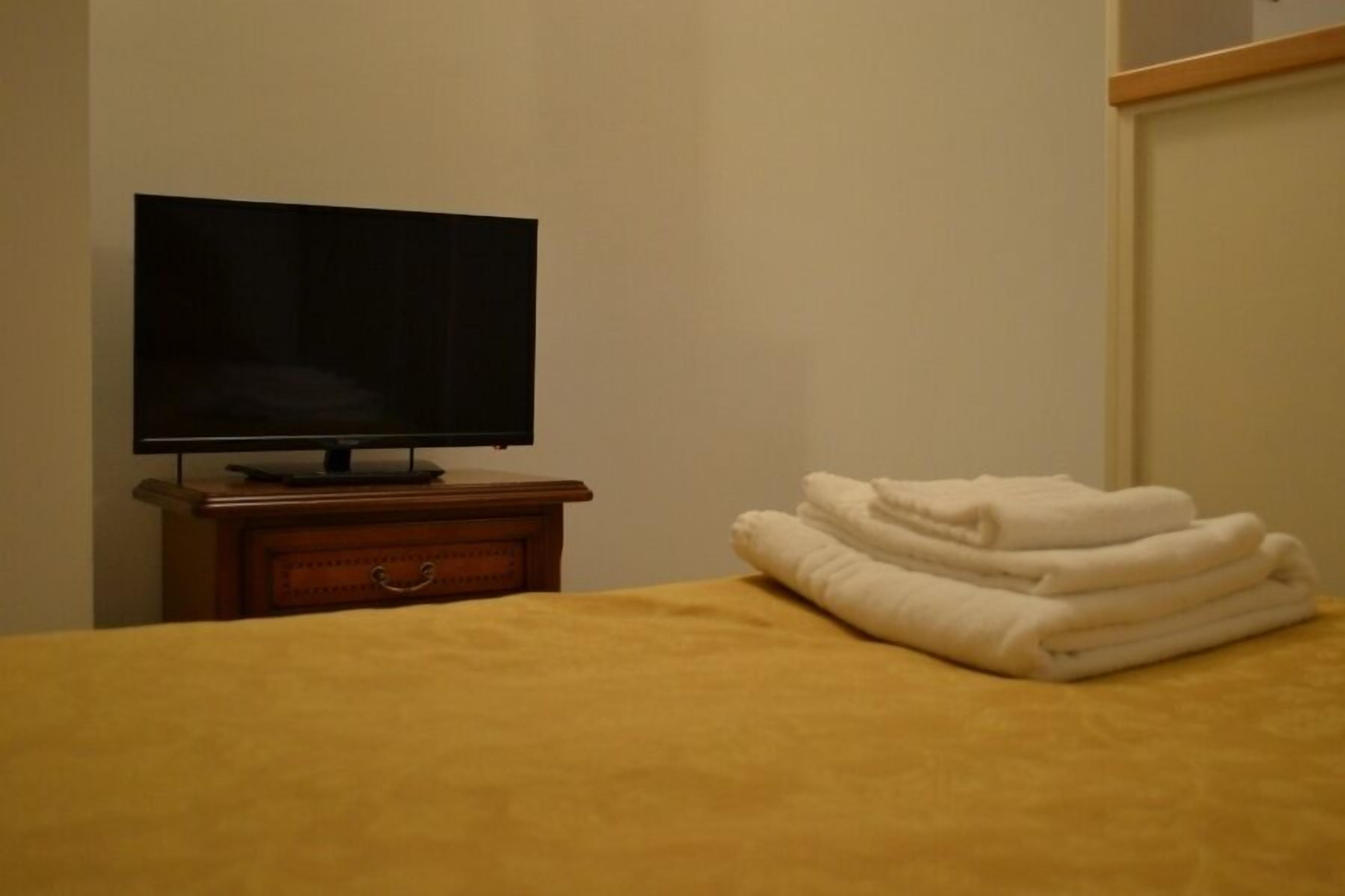A hotel room with a bed, a television on a wooden stand, and a stack of white towels.