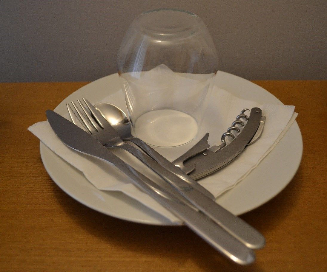 Une table dressée avec une assiette, des couverts, un verre et une serviette sur une table en bois.