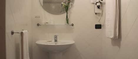 A bathroom with a pedestal sink, a round mirror, a towel rack, and a telephone.