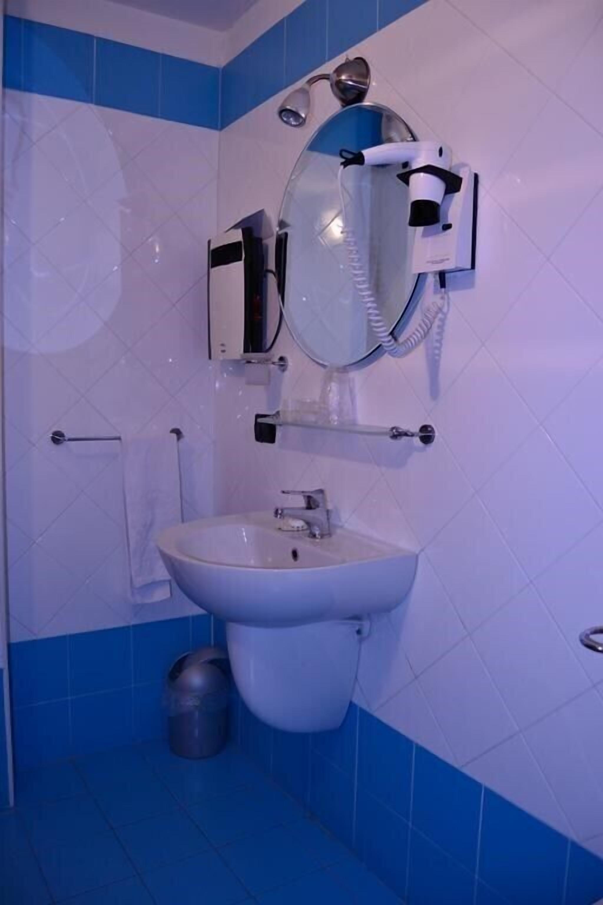 A bathroom with a white sink, a mirror, and a hairdryer mounted on the wall.