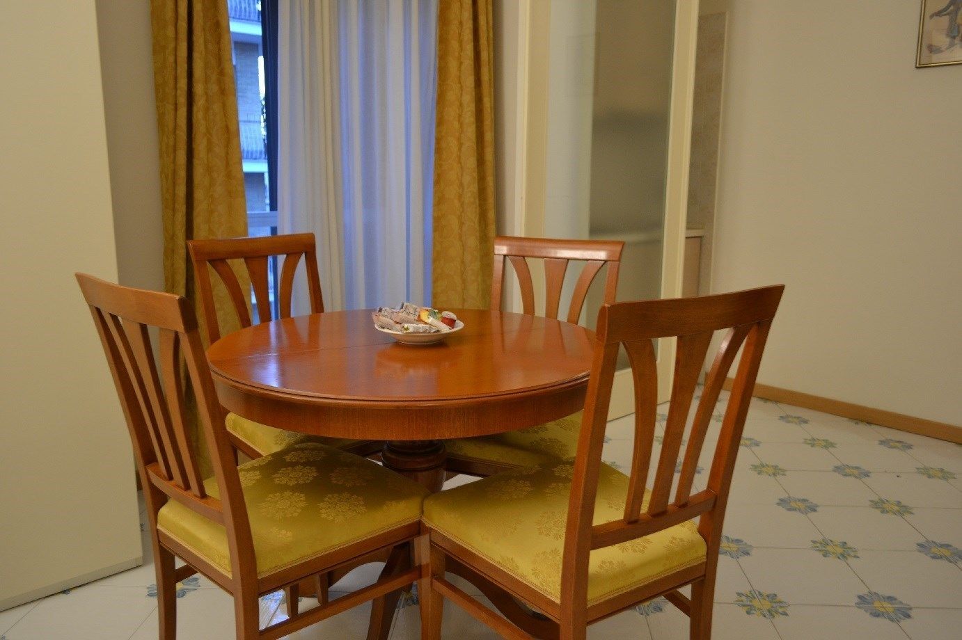 A round wooden dining table with four chairs, each with a yellow cushioned seat.