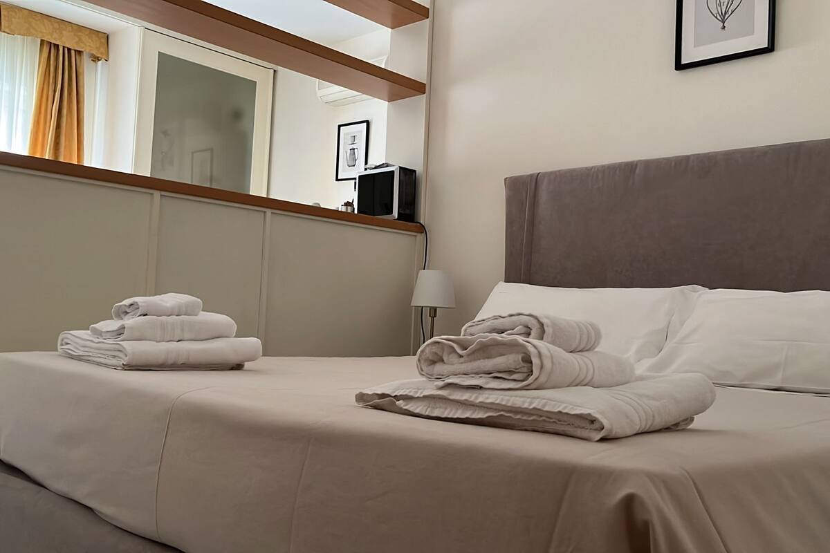 Cama bem arrumada com toalhas dobradas, abajur e quadro na parede.