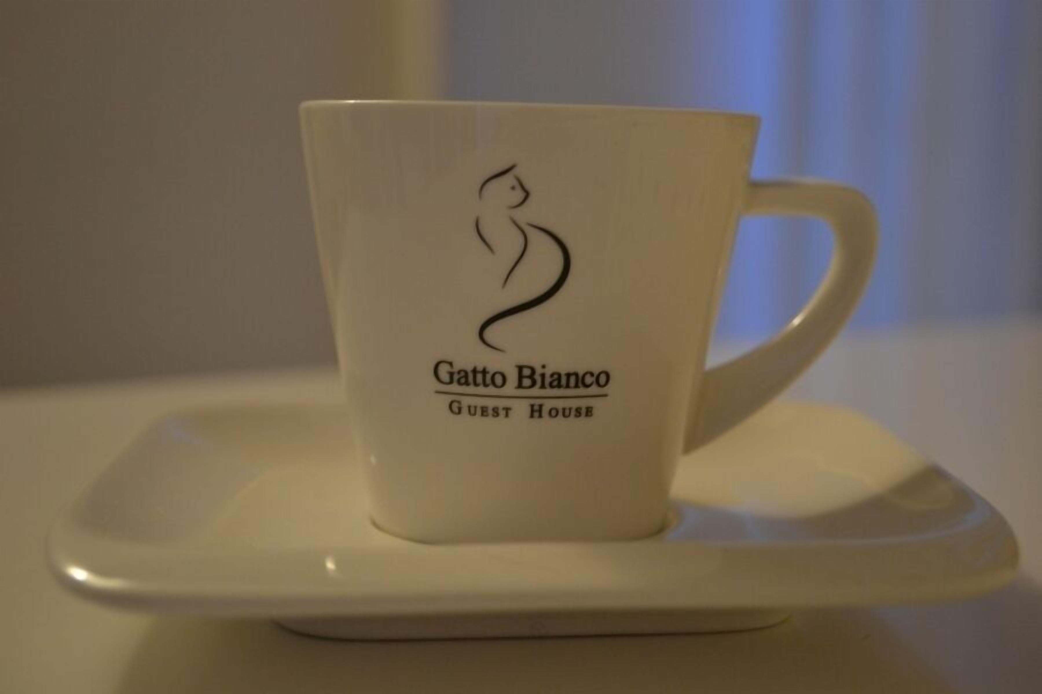 Una taza de cerámica blanca con un logotipo y texto, sobre un platito blanco.