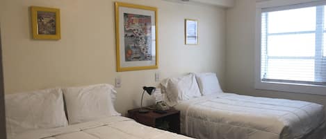 Quarto de hotel com duas camas, uma mesa de cabeceira com abajur e uma janela com persianas.