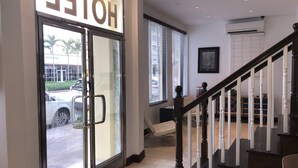 A hotel entrance with a glass door, a staircase with white balusters, and a view of parked cars outside. - Hotel Ponce de Leon (Coral Gables)
