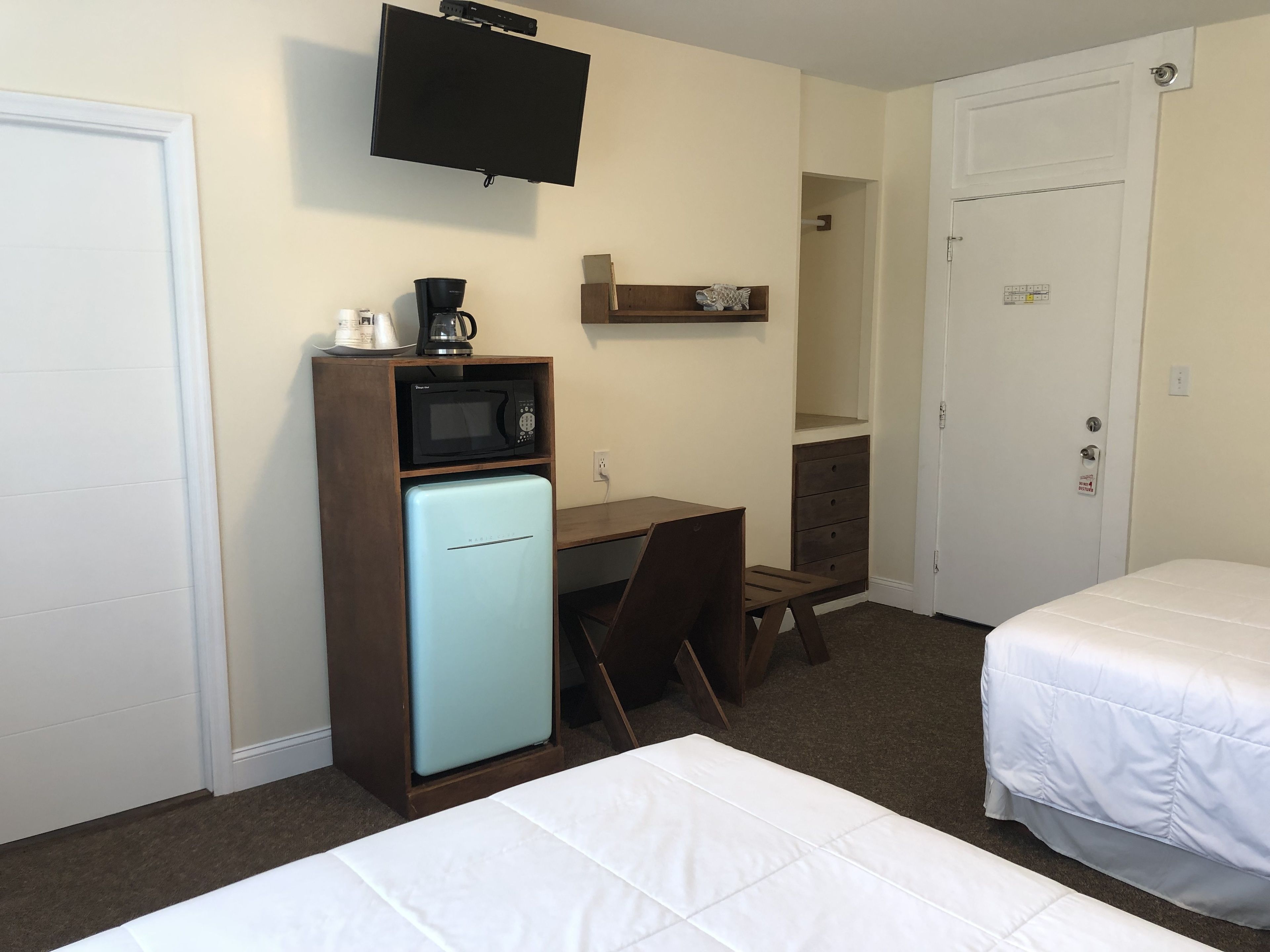 Habitación de hotel con cama, escritorio con microondas, cafetera y televisor montado en la pared.