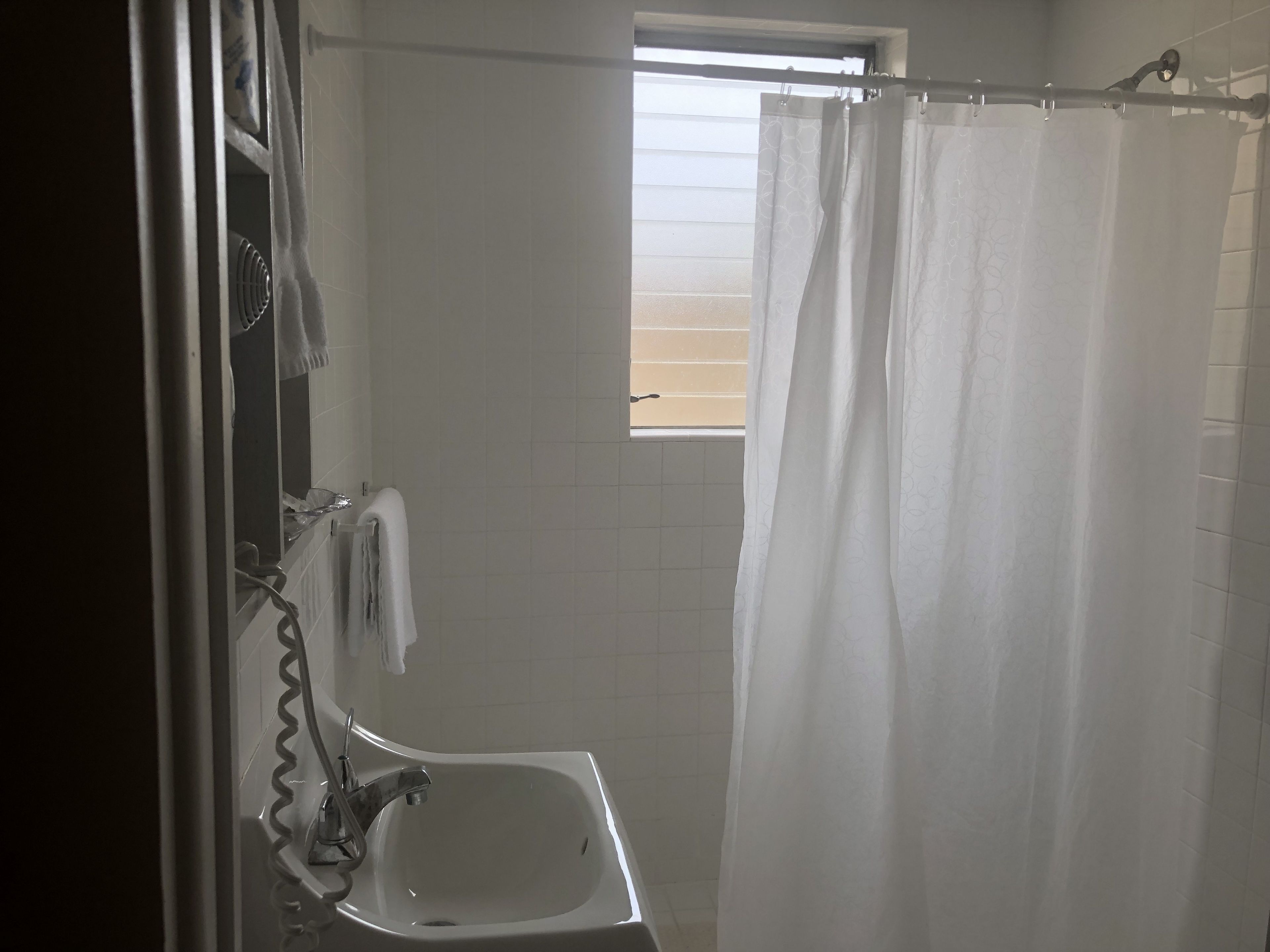 Un baño con lavamanos blanco, espejo y cortina de ducha.