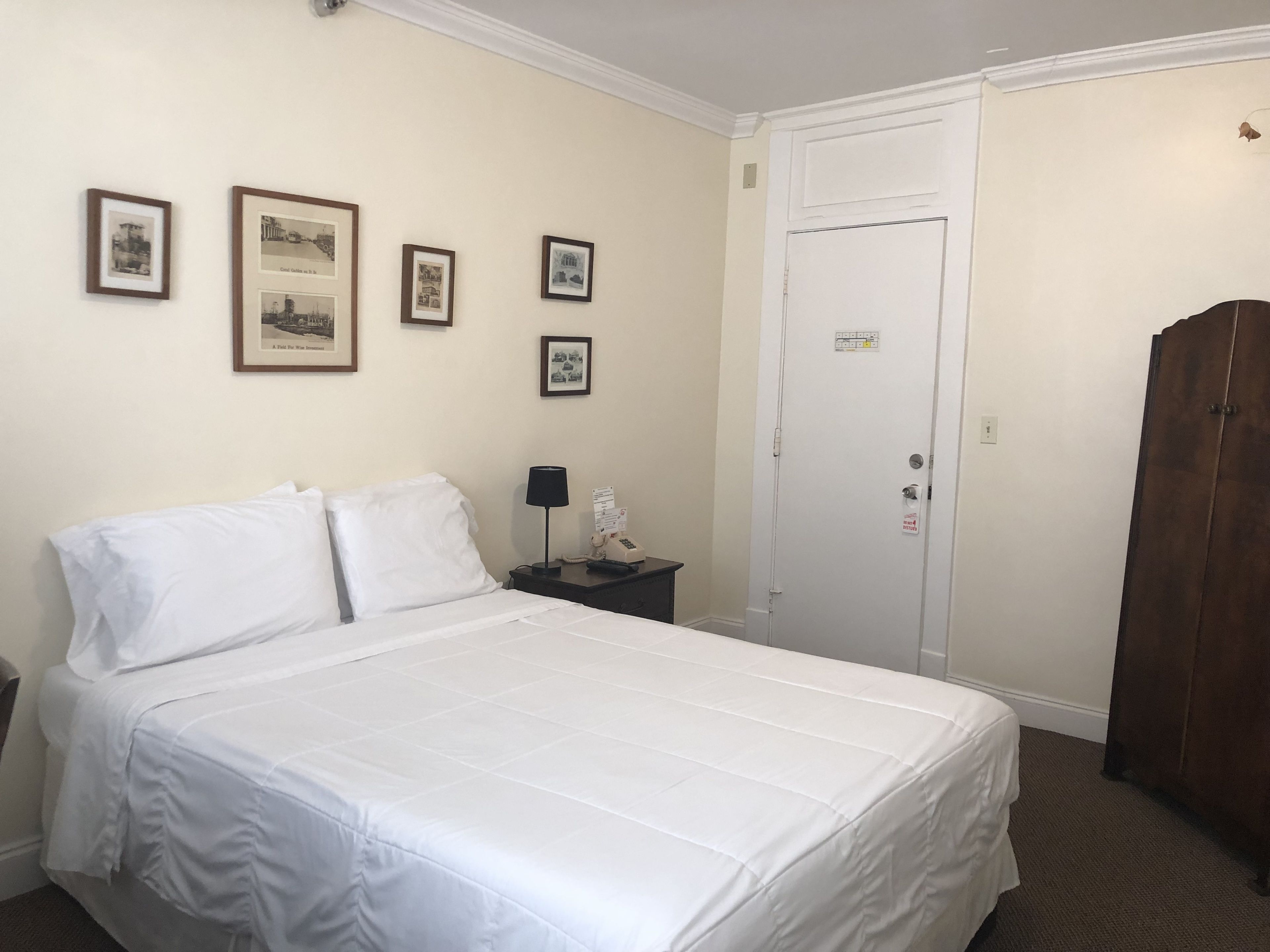 Une chambre d’hôtel avec un lit, une table de chevet, une lampe, une armoire et des tableaux encadrés au mur.