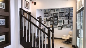 A staircase with dark wooden balusters and a white handrail, leading to a landing with a seating area and a wall adorned with numerous framed black and white photographs. - Hotel Ponce de Leon (Coral Gables)