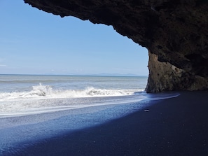 Una playa con arena oscura y olas rompiendo contra las rocas.