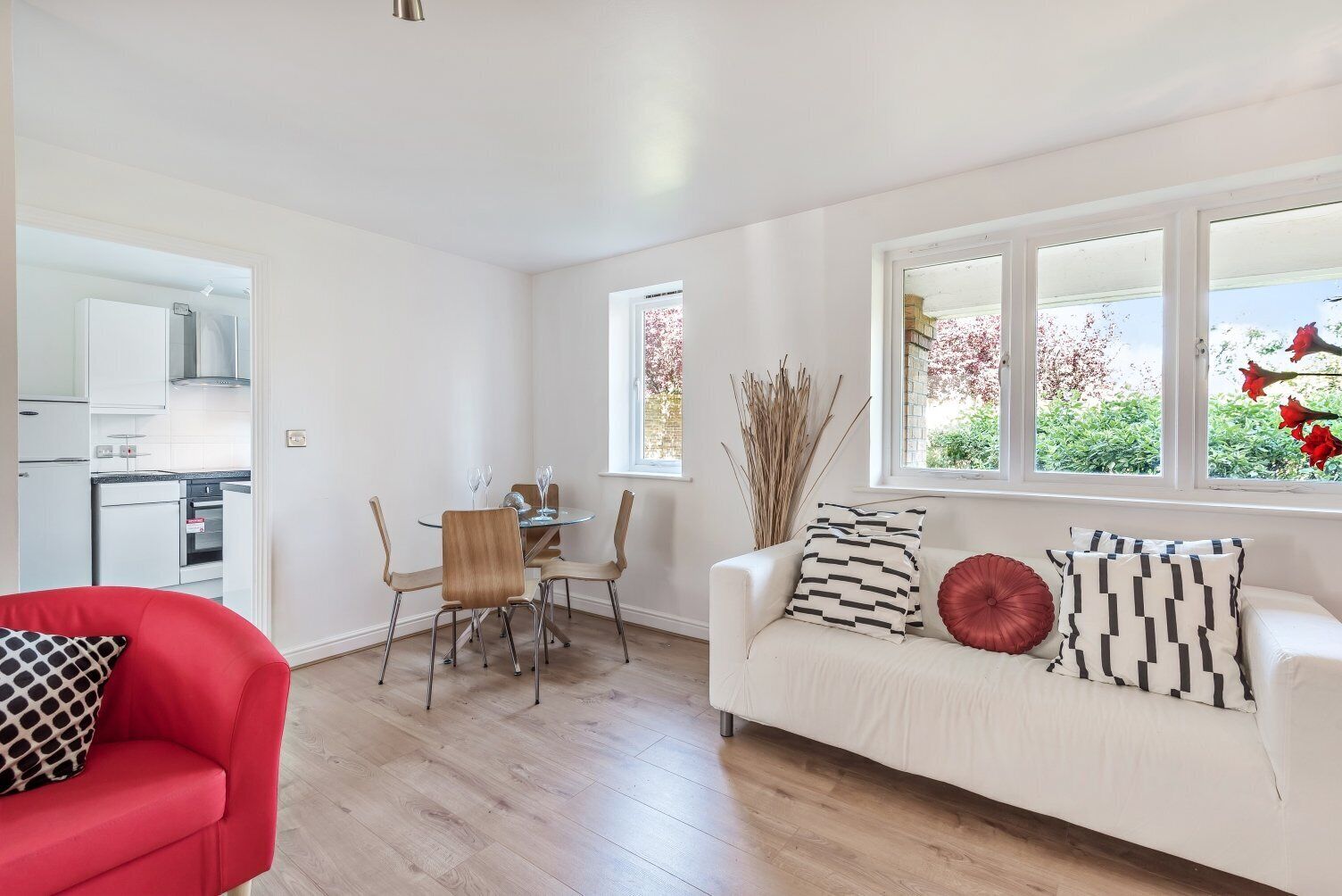 A modern living room with a white sofa, red armchair, and a dining area with a table and chairs.