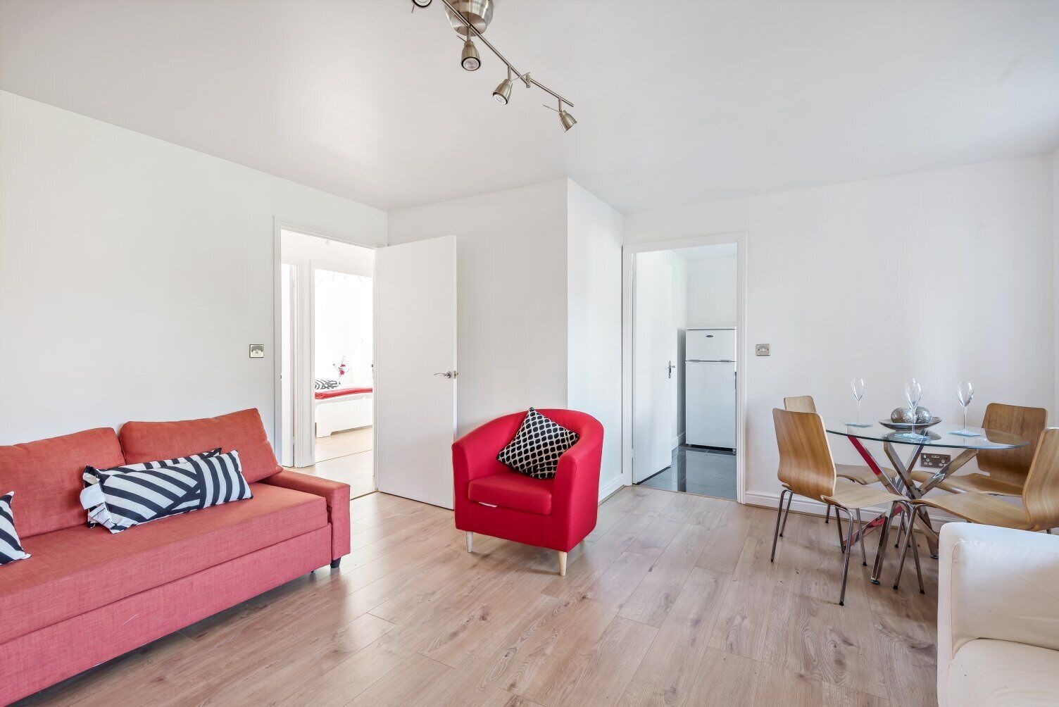 Ein modernes Wohnzimmer mit einem roten Sofa, einem roten Sessel und einem Essbereich mit einem Glastisch und Stühlen.