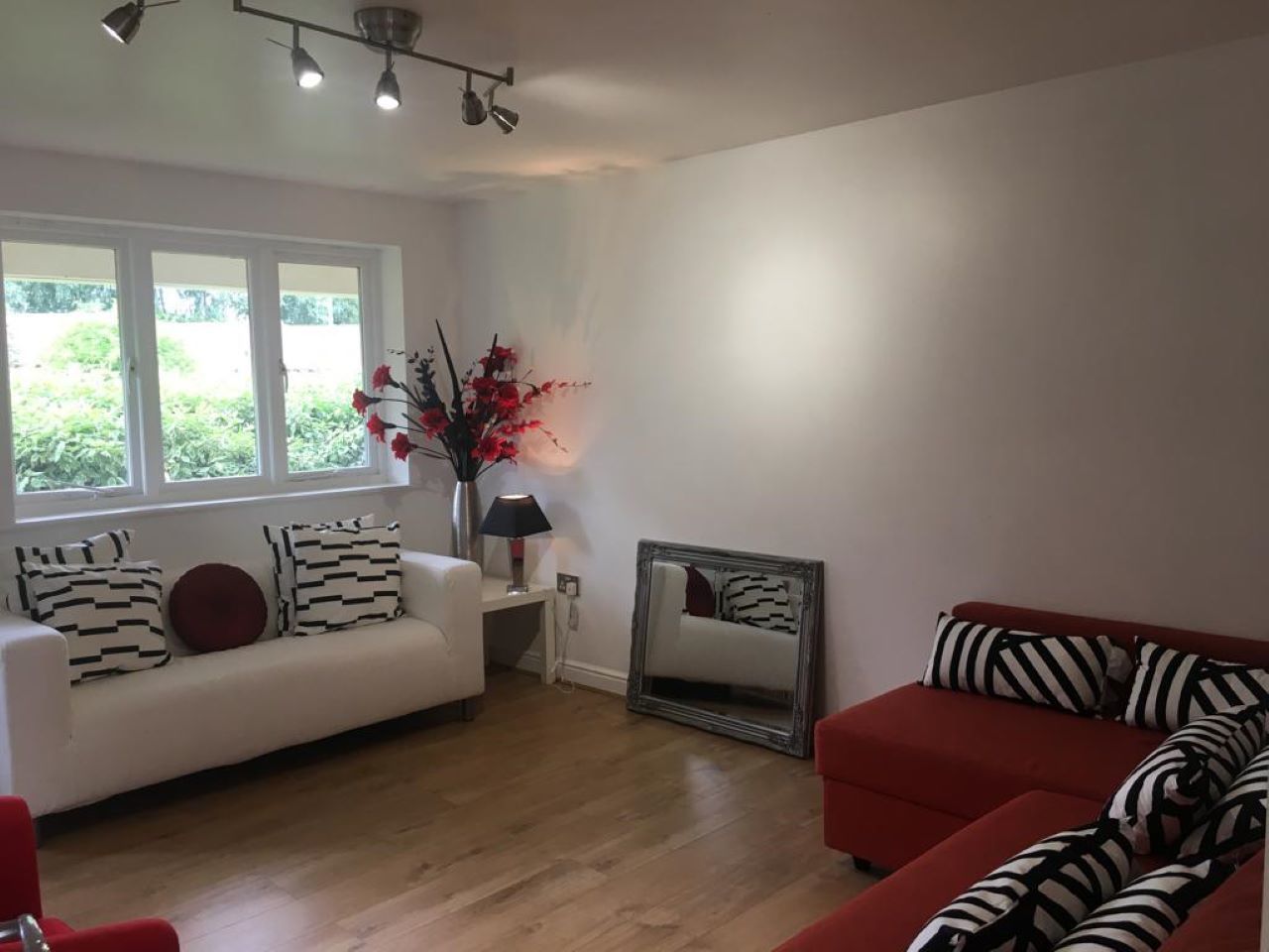 A living room with a white sofa, a red sofa, a mirror, and a vase with flowers.