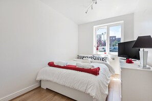 A bedroom with a bed, a TV, and a window with a view of buildings. - Triple-Train Hub | Step-Free | Parking | Pets (London)