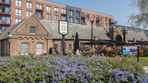 A building with a brick facade, a signboard, and a flower garden in front. - 2 Bed Flat, Dedicated Workspace, Parking, 4KTV (London)