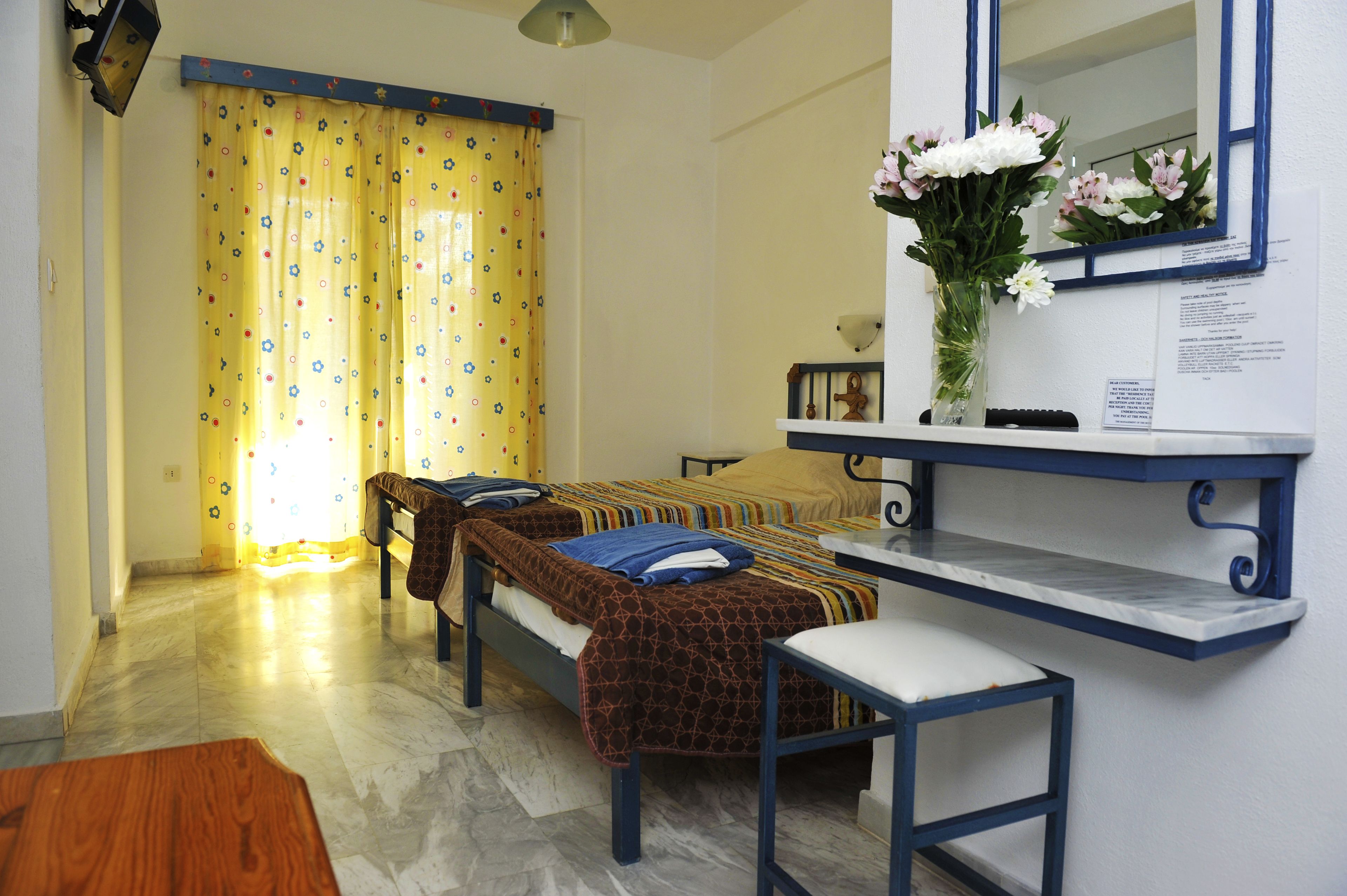 Ein Zimmer mit zwei Betten, einem kleinen Tisch, einem Spiegel und einer Vase mit Blumen.